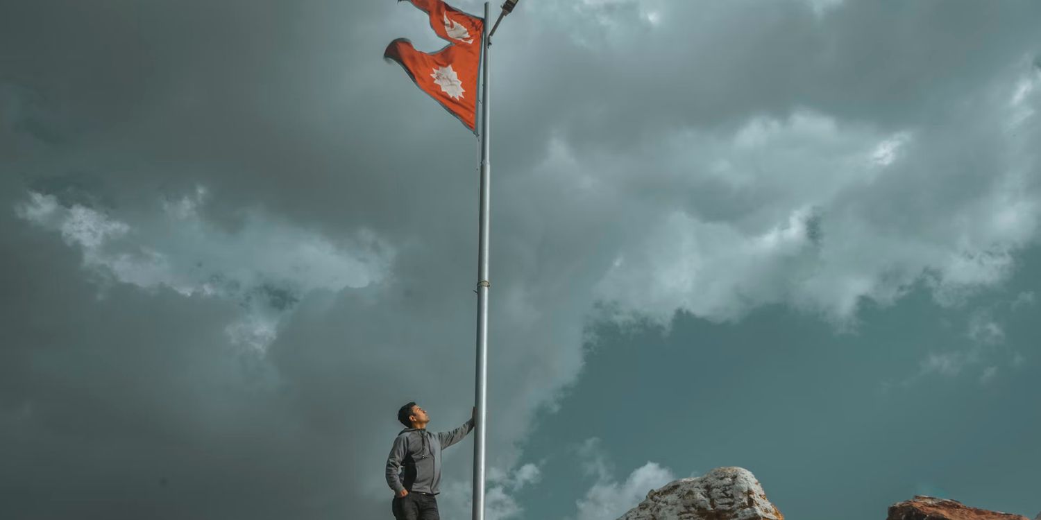 man-at-the-base-of-a-flagpole-flying-the-flag-of-nepal